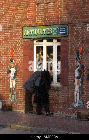 Una coppia in cerca nella finestra di un negozio di antiquariato atEpicerie a Beuvron En Auge Normandia Francia Foto Stock