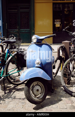 Vecchia Vespa blu con fango dinted guard e graffi parcheggiata tra le biciclette per le strade di Parigi Foto Stock