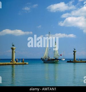 Ingresso mozzafiato per Mandraki Harbour con alte colonne in pietra su entrambi i lati e nave a vela lasciando Rodi Isole greche Foto Stock