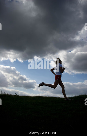 Esecuzione di una donna come una silhouette di fronte a un cielo di nuvole scure Foto Stock