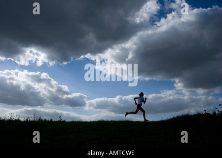 Esecuzione di una donna come una silhouette di fronte a un cielo di nuvole scure Foto Stock