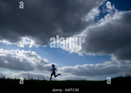 Esecuzione di una donna come una silhouette di fronte a un cielo di nuvole scure Foto Stock