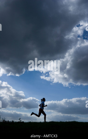 Esecuzione di una donna come una silhouette di fronte a un cielo di nuvole scure Foto Stock