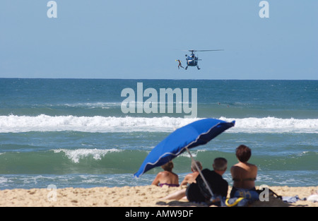 Elicottero francese per il salvataggio aereo in mare che fa cadere un bagnino nel mare. I villeggianti guardano sulla spiaggia da sotto un ombrellone. Messange spiaggia Francia Foto Stock