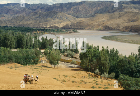 CHINA Ningxia il Fiume Giallo e piegare nella regione di sabbia del nord ovest della Cina con i turisti in giro in cammello e montagne Foto Stock