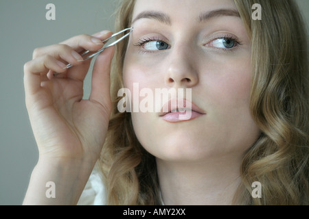 La riflessione di giovane donna servendosi di pinzette per sopracciglia Foto Stock