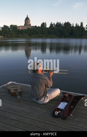 L'uomo gioca Trombone sul Dock al tramonto Lago Capitol Olympia Washington Washington State Capitol Building in background Foto Stock