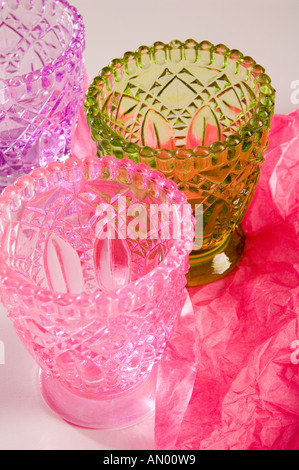 Set di tre il vetro pressato multi-bicchieri colorati, essendo avvolto in rosa carta tessuto per un regalo. Girato su uno sfondo bianco. Foto Stock