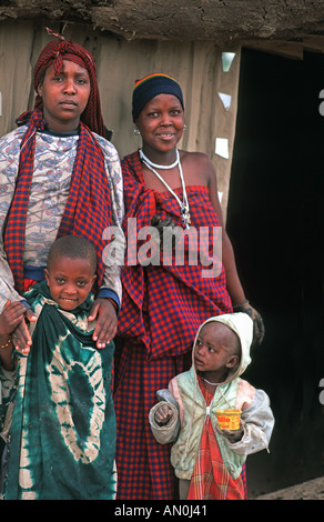 Masai mamme con bambini avvolti in tessuti al di fuori del loro fango e legno home N di Arusha in rotta verso S Kenya Tanzania Foto Stock