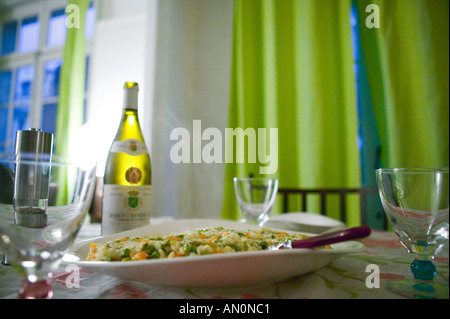 Una piastra di cottura a vapore del risotto con carrotts e piselli sorge su una tabella in un appartamento accanto ad una bottiglia di vino bianco 2005 Foto Stock