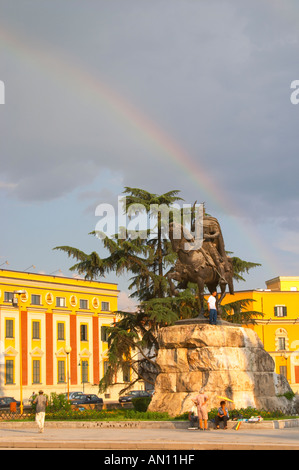 La statua del xv secolo un guerriero e un eroe nazionale Skanderbeg Skanderburg su un enorme base di pietra. Un colorato arcobaleno nel cielo e edifici amministrativi in background. Il Tirana Piazza Centrale, Skanderburg Skanderbeg Square. Organizzazione turistica nazionale in background. Capitale Tirana. L'Albania, Balcani, Europa. Foto Stock