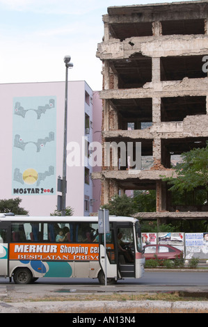 Scena di strada con bus di " commuters ". Edificio a Mostar danneggiata dalla guerra e non ancora rinnovate. Rovinato dai fori di proiettile, Malta bomba granata shell danni, molto vicino al splendidamente rinnovato centro storico centro citta'. Facciata di edificio che commemora la ricostruzione del ponte in 2004. Città di Mostar. Federazione Bosne i Hercegovine. La Bosnia Erzegovina, l'Europa. Foto Stock