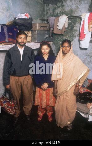 Gruppo di famiglia in piedi in camera da letto, con le valigie su un ripiano e macchie sul muro. India Foto Stock