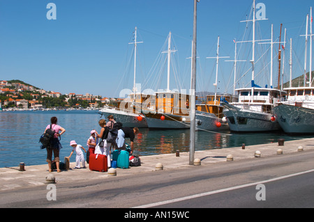 Una fila di bella crociera in legno, barca a vela e barche da pesca di navi Barche dipinte di bianco ormeggiate lungo che la chiave nel porto. Una famiglia in attesa presso la keyside con diverse borse e valigie. Luka porto di Gruz. Dubrovnik, città nuova. Costa della Dalmazia, Croazia, Europa. Foto Stock