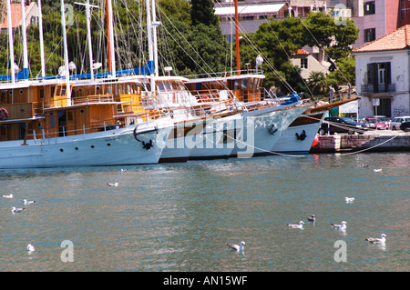 Una fila di bella crociera in legno, barca a vela e barche da pesca di navi Barche dipinte di bianco ormeggiate lungo che la chiave nel porto. Gli archetti delle navi schierate e riflessa nell'acqua. Luka porto di Gruz. Dubrovnik, città nuova. Costa della Dalmazia, Croazia, Europa. Foto Stock