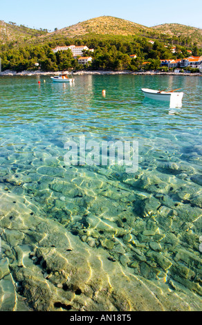 Vista su tutta la baia di Brna con riflessi di luce nell'acqua. Acqua molto limpida così potete vedere le formazioni rocciose a fondo semitrasparente. Barche ormeggiate presso una boa. Montagne sullo sfondo. Prizba village. Isola di Korcula. Prizba, gli appartamenti Riva, Danny Franulovic. Isola di Korcula. Costa della Dalmazia, Croazia, Europa. Foto Stock