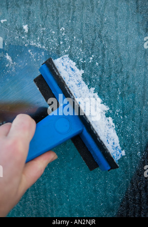 La raschiatura di ghiaccio da un parabrezza di automobile con un raschiatore Foto Stock