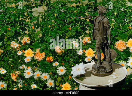 Un'antica statua di piombo di un giovane uomo sorge in un birdbath nel giardino di rose, Missouri USA Foto Stock