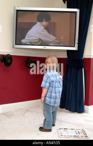 Bambino guardando la televisione Little Boy in piedi. Televisore montato sulla parete. Foto Stock