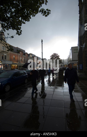 Gli amanti dello shopping a piedi con ombrelloni sulla pioggia inzuppato Main Street, Llandudno North Wales UK Foto Stock