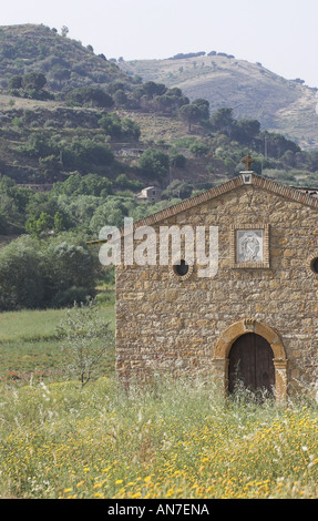 Una semplice vecchia chiesa di pietra impostare un campo di giallo fiori selvatici situato in una valle tra le colline della Sicilia Foto Stock