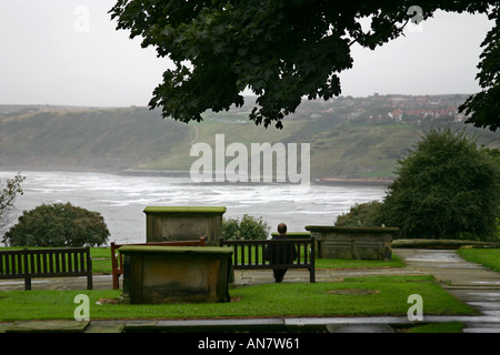 Uomo seduto sul sedile nella chiesa cimitero affacciato sul South Bay a Scarborough North Yorkshire Foto Stock