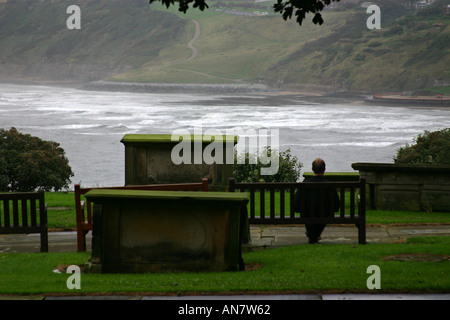 Uomo seduto sul sedile nella chiesa cimitero affacciato sul South Bay a Scarborough North Yorkshire Foto Stock