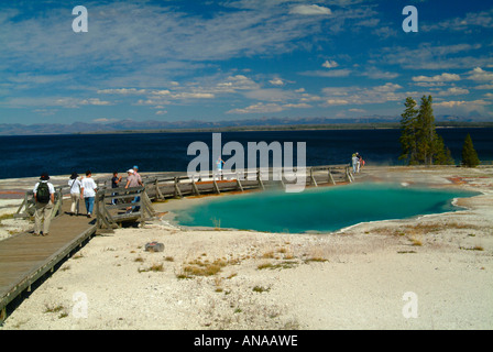 Turisti che si godono di vista piscina nero in primavera in West Thumb Geyser Basin nel Parco Nazionale di Yellowstone Wyoming USA Foto Stock