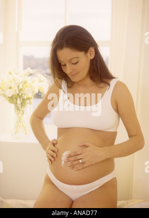 Donna fortemente incinta che applica crema idratante alla pancia per aiutare a prevenire le smagliature, Regno Unito Foto Stock