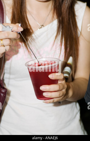 Metà vista in sezione della giovane donna Holding e agitazione Red Cocktail di benvenuto Foto Stock