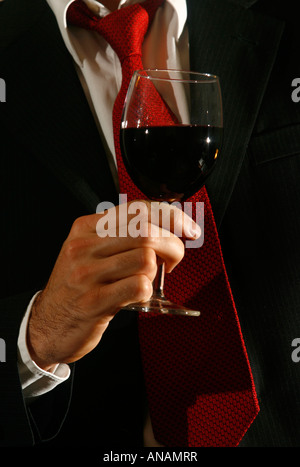 Uomo in un vestito e un tirante tiene un bicchiere di vino rosso Foto Stock