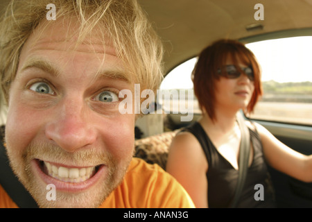 Giovane biondo uomo con la fidanzata facendo un autoritratto in un'auto in movimento Foto Stock