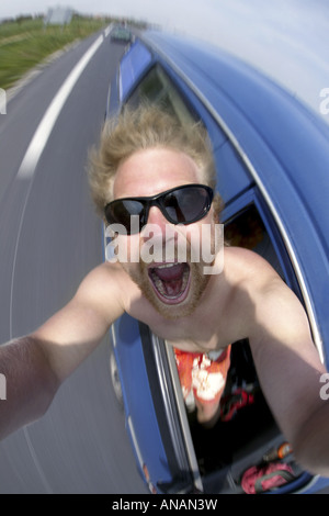 Giovane biondo Uomo con occhiali da sole rendendo un autoritratto in un'auto in movimento Foto Stock