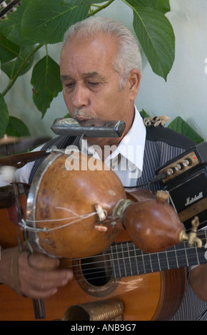 Uomo a suonare la chitarra (con erogatore di rum allegata) e armonica a bocca al Fiesta su Gran Canaria Foto Stock