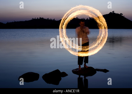 Uomo fuoco danza su una roccia in un lago in India Foto Stock