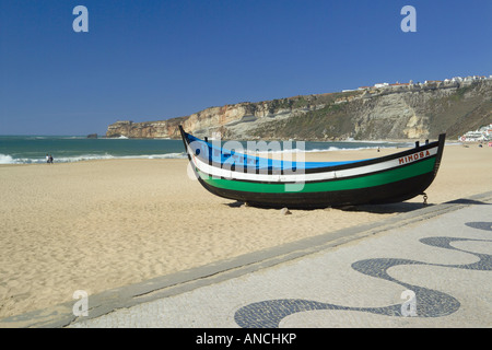 Il Portogallo, la Costa Da Prata, Nazaré beach, una barca da pesca e tipico portoghese ciottoli decorati marciapiede sul lungomare Foto Stock