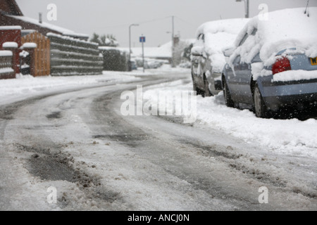 Tracce di pneumatici vettura e marchi in mezzo alla strada in curva della coperta di neve street con ghiaccio granite e automobili parcheggiate Foto Stock