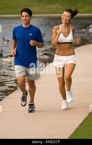 Una giovane coppia asiatica ispanica e jogging accanto a un lago in un parco Foto Stock