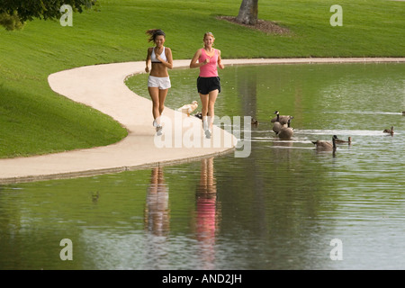 Due giovani donne asiatiche e caucasiche jogging accanto a un lago in un parco Foto Stock