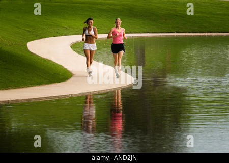 Due giovani donne asiatiche e caucasiche jogging accanto a un lago in un parco Foto Stock