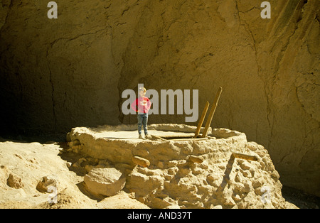 Un giovane ragazzo si arrampica in un antico Anasazi kiva o camera di religiosi in una grotta in Bandelier Foto Stock