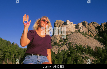 Una donna con una bandiera americana dipinta sulla sua mano si siede di fronte a Monte Rushmore National Memorial Foto Stock