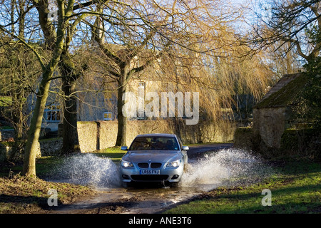 La BMW Serie 5 unità auto attraverso il vicolo del paese ford Swinbrook Oxfordshire, Regno Unito Foto Stock