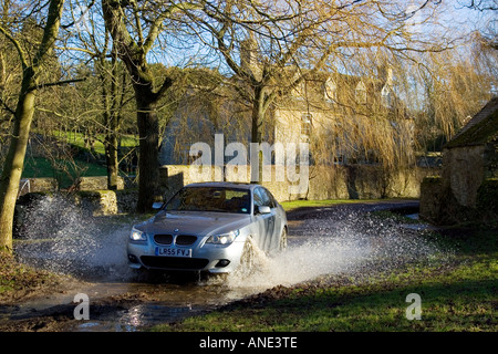 La BMW Serie 5 unità auto attraverso il vicolo del paese ford Swinbrook Oxfordshire, Regno Unito Foto Stock