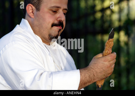 Chef in uniforme preme Carni bovine su uno spiedino Foto Stock