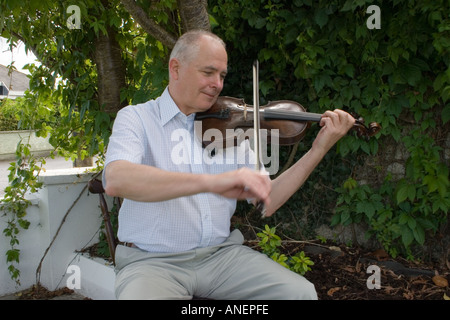 Uomo inglese suona il violino all'aperto seduto sotto un albero. La musica tradizionale irlandese. Tipperary, Irlanda Foto Stock