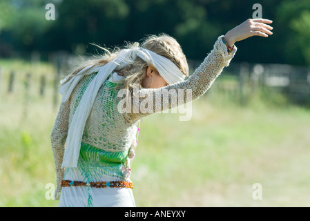 Giovane donna in sundress in piedi in campo con il braccio in alto, guardando verso il basso Foto Stock