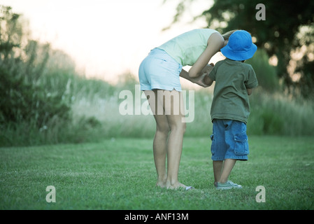 La madre e il figlio in piedi sul prato, donna di piegarsi per parlare al ragazzo Foto Stock
