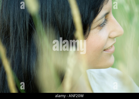 Donna sorridente, guardando lontano, offuscata la vegetazione in primo piano Foto Stock