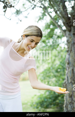 Donna in piedi all'aperto, tenendo fetta d'arancia nel palmo della mano Foto Stock